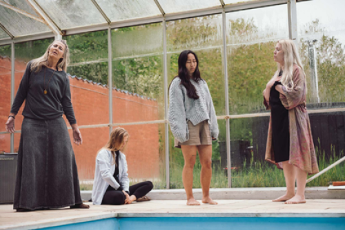 Flere personer på psykoterapeutuddannelse deltager i en kropsbaseret øvelse i et lyst drivhusmiljø – illustrerer nærvær, grounding og personlig udvikling som en del af Tobias‑Skolens psykoterapeutuddannelse, kurser og efteruddannelser på Sjælland og i Jylland.