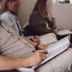 Person der tager noter i en notesbog under undervisning – stemningsbillede der illustrerer fordybelse, læring og den professionelle tilgang på Tobias‑Skolens psykoterapeutuddannelse og efteruddannelser.