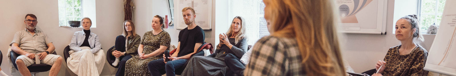 Gruppe af voksne deltagere i undervisningslokale under psykoterapi‑uddannelse hos Tobias-Skolen, med fokus på dialog, refleksion og fællesskab